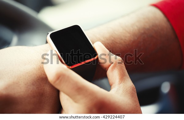 Hands of african male model
using trendy smart wrist watches in a car. Popular new technology
to always stay connected to internet and social media. Close up
macro 