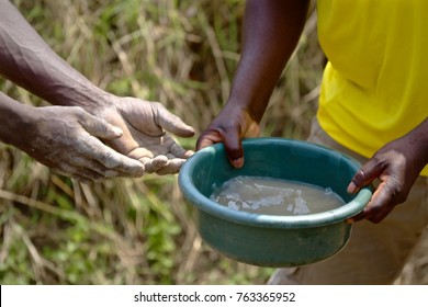 The hands of African men are shown holding a bucket of dirty water.  Cholera is a major problem in Malawi, due to the lack of access to clean drinking water.