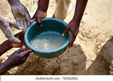 The Hands Of African Men Are Shown Passing A Bucket Of Dirty Water.