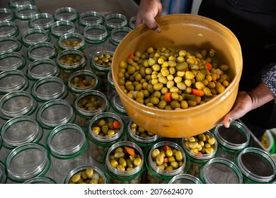 Hands of African worker filling glass jars with pickled green olives in packaging shop at factory
