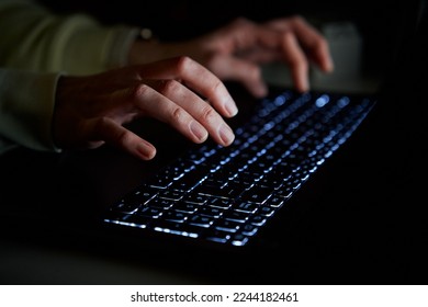 Hands of anonymous person typing on laptop keyboard at night, close up. Cyber security concept