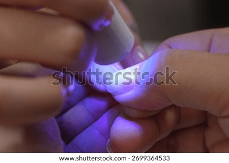 Hands applying a base coat or clear builder gel on a woman's natural fingernail, using a handheld UV lamp for polymerization during a beauty session