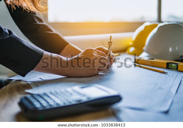 Hands\
of architect enginering holding divider compass with working\
blueprints for inspection in workplace construction project in\
office. Engineering tools and construction\
concept.