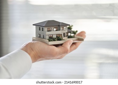 Hands of an Asian man holding an architectural model of a single house - Powered by Shutterstock