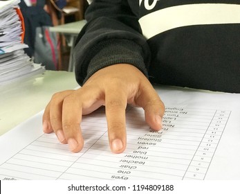 The hands of asian student pointing the English vocabulary in the worksheet for reading test on teacher's table with Sheet pile. 