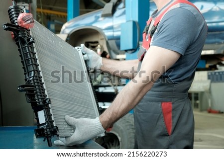 In the hands of an auto mechanic, an automobile radiator. Inspection and control of compliance, integrity of the spare part. Repair and maintenance in the car center.