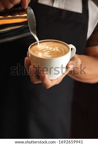 Hands of a barista pouring warm milk into a cappuccino or latte making a pattern of milk into coffee.