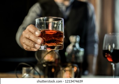 Hands of a bartender, with a glass of whiskey, soft focus.