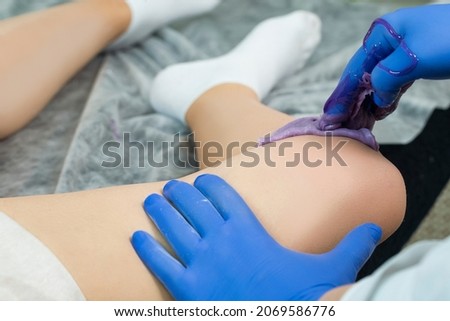 Hands of a Beautician During Depilation With Hot Wax On Female Legs In Beauty Spa Salon While Body Hair Removal With Epilation.Horizontal Shot