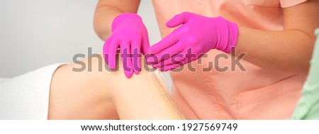 Hands of a beautician in pink gloves epilating leg of a young female in hair removal salon