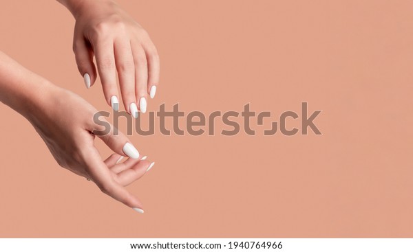Hands of a\
beautiful well-groomed woman with feminine nails on a beige\
background. Manicure, pedicure beauty salon concept. Empty space\
for text or logo. On nails white gel\
polish