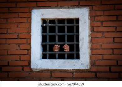 Hands behind the bars in a brick prison. Prisoner in a Far-Western style set.