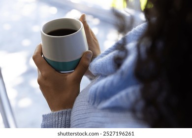 Hands of biracial woman holding cup of coffee and looking out window at home. Lifestyle, free time and domestic life, unaltered. - Powered by Shutterstock