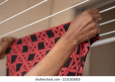 Hands of black brazilian lady extending her clothes with clothespin on fingers on clothesline in laundry