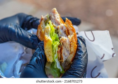 Hands In Black Disposable Gloves Are Holding Hamburger. Half Of