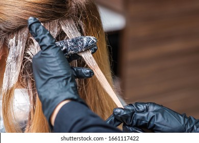 Hands in black gloves dye hair of woman in hair salon, hair coloring process.