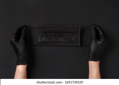 Hands in black latex gloves. Black face mask on a black background. Sterile gloves. Antiviral protection in a coronavirus pandemic. Space for text.