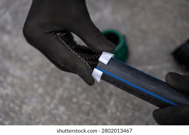 Hands in black protective work gloves installing a white plastic compression ring onto a black HDPE pipe with a blue stripe, assembly process of water supply pipeline system.