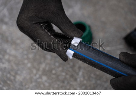 Hands in black protective work gloves installing a white plastic compression ring onto a black HDPE pipe with a blue stripe, assembly process of water supply pipeline system.