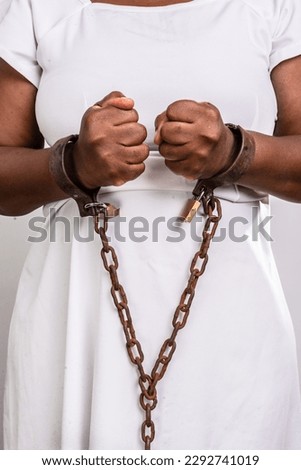 Hands of a black woman chained with old rusty iron chain and padlock. Slave trade prevention concept.