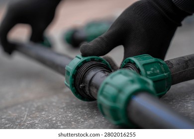 Hands in black work gloves assembling a plastic compression tee fitting connected to three HDPE pipes, installing a pipeline branch system for water supply or irrigation.