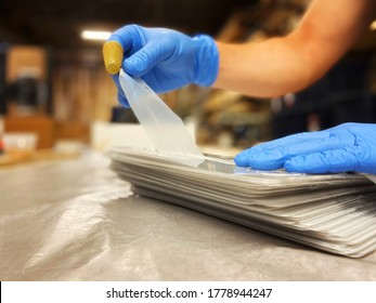 Hands In Blue Gloves Ripping The Film Of The Stack Of Clear Plastic Shields