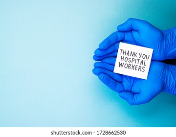 Hands In Blue Medical Gloves Holding The Inscription Thank You To The Hospital Workers, Top View. Thanks To The Medical Staff, Doctors And Nurses