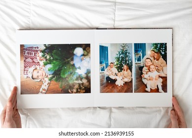 Hands With Book With New Year Photos Of Big Family At Home On A White Background. Photobook Is Gift. Professional Photographer And Designer. Printing Of Photos And Journals In Photo Laboratory