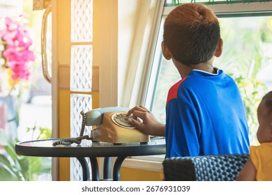 Hands of boy try to using old phone or dial telephone. Boy curious and tried using old rotary phone or dial phone. Curious child play with antique vintage rotary old landline phone. Old fashioned.