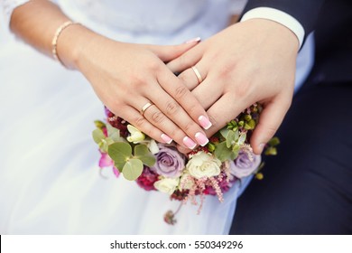 Hands of bride and groom with rings on wedding bouquet. Marriage concept.
