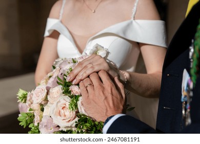 Hands of bride and groom with wedding rings on beautiful bouquet of roses. A bride and a groom holding hand and showing up the wedding ring.  - Powered by Shutterstock