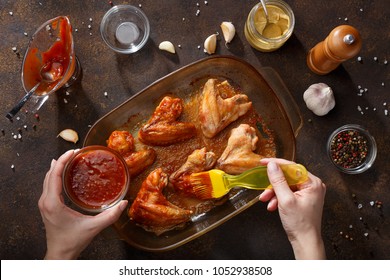 Hands brush baked wings with the bbq souce. Step by step recipe of homemade bbq wings top view.