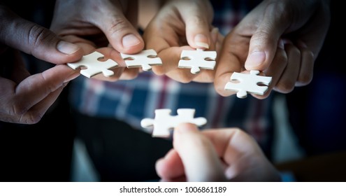 Hands of business people wearing casual plaid shirt hold paper jigsaw puzzle and solving puzzle together,Business team assembling Jigsaw puzzle,Business group wanting to put pieces of puzzle together.