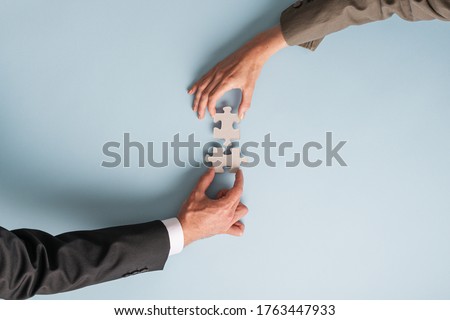 Hands of a businessman and businesswoman joining two puzzle pieces in a conceptual image of merger and partnership.