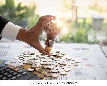 Hands Of Businessman Holding A Light Bulb With Coin. The Idea Of ​​reducing Costs And Reduce Energy Consumption And Energy Savings