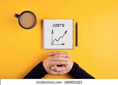 Hands of a businessman and a spiral notebook with the word costs written on it. Increasing or rising business costs. - Powered by Shutterstock