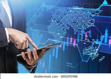Hands of businessman using tablet over blurry blue background with double exposure of world map and graph. Toned image