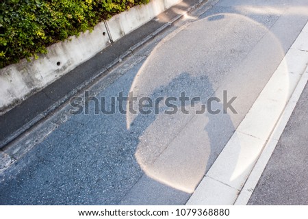 Hands and a camera being held through a beam of light (mirror refection) and create a shadow on the road.