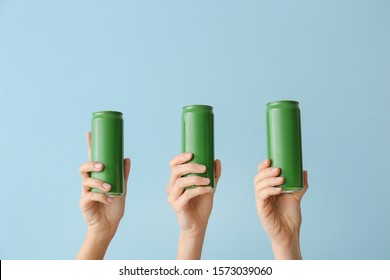 Hands with cans of beer on color background