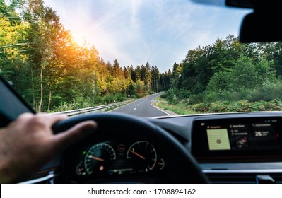 Hands of car driver on steering wheel, fast driving car at spring day on a country road, having fun driving the empty highway on tour journey - POV first person view shot