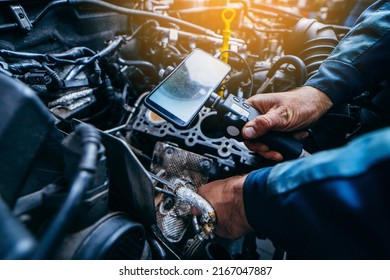 Hands Of Car Mechanic Check The Vehicle Engine With Technical Endoscope With Rotary Camera And Mobile Phone. Repair Of Engine Head And Valves.