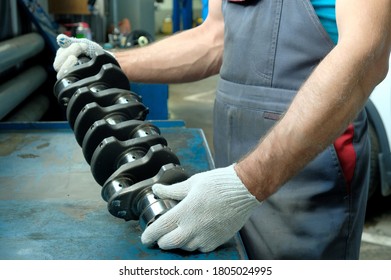 In the hands of a car mechanic, a new crankshaft. Car engine repair. The quality of the spare part is checked before it is installed.