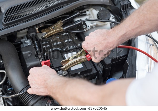 Hands\
of car mechanic using cables to start a car\
engine
