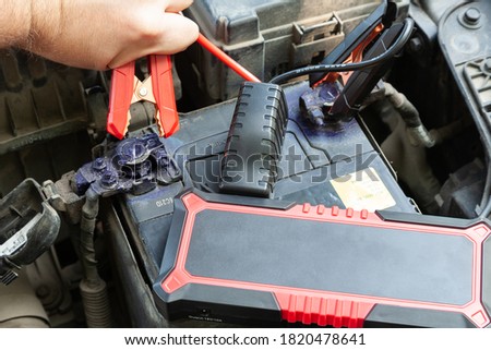 Hands of car mechanic using portable car jump starter to start-up engine. Close up view.
