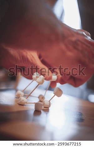 Hands carefully assemble a structure using toothpicks and mini marshmallows, focusing on creativity, teamwork, and problem-solving in a hands-on activity.