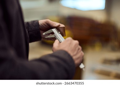 Hands carefully measuring an object in a workshop setting with calipers.