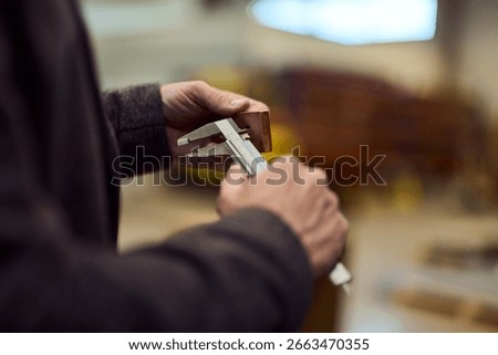 Hands carefully measuring an object in a workshop setting with calipers.
