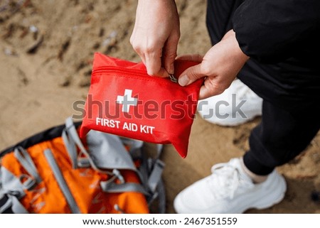 Hands carefully preparing a first aid kit on a sandy beach, emphasizing the importance of outdoor safety and emergency preparedness. Backpack in the background for travel health and protection