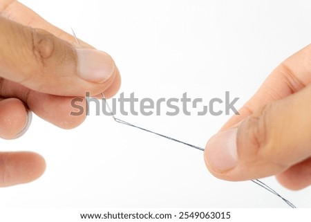 hands carefully threading a needle with dark thread against a white background.