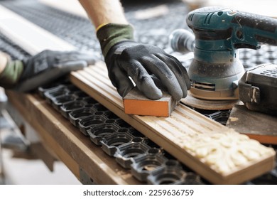 Hands of a carpenter manually sanding the edge of a wooden block with sandpaper on a hand tool in a woodworking or carpentry workshop - Powered by Shutterstock